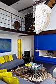 Ein blauer Kamin und gelbe Wohnaccessoires bestimmen den modernen Stil dieses offenen Wohnraums mit Galerie
