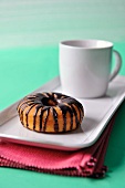 A doughnut with chocolate glaze and a cup