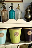 Antique soda siphons of different colours and glazed pots with royal seal on nostalgic, wall-mounted shelves with curved front panel