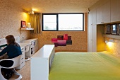 Woman sitting at desk in bedroom opposite bed with light green bedspread