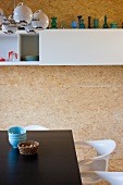 Black dining table and white chairs in front of white overhead cupboard on chipboard-clad wall