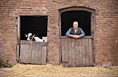 A farmer and a calf looking over barn doors
