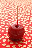 A toffee apple on a red, heart-patterned surface