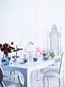 Antique style white upholstered chairs at a romantic white table laid with pastel china, cake stand and glass covers