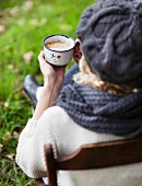 A woman with a cup of coffee on a chair outdoors