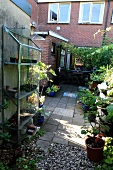 Allotment ambiance with plant nursery in front of paved and gravel terrace area of house with exposed brickwork and summery vintage character