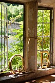 Zwei goldene Dekobuchstaben von der Sonne angestrahlt, stehen auf einem Fenstersims aus Stein vor geöffneten Vintage Sprossenfenstern aus Metall