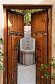 View through an open wooden door of a tiled hand basin in a courtyard