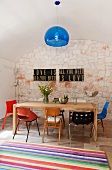 Eine Sammlung von Designer-Stühlen des 20. Jahrhunderts um einen hölzernen Esstisch in der Küche mit blauer transparenter Pendelleuchte und gestreiftem Teppich