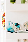 Blue glass vases and painted china plates on white shelves
