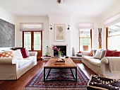 Pale sofas with scatter cushions and retro table on Oriental carpet in bright living room
