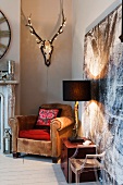 Fairy lights adorn a mounted stag head with antlers on wall above vintage leather armchair