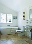 Bright, spacious bathroom under the sloping roof with modern bathtub, stone tiles and large window