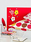 Artistic, 70s-style headboard with flowers, wooden beads and matching pillow covers on bed; tabletop mirror and French literature on bedside table