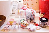 Sweets and sewing utensils in storage jars, Japanese doll, teacup and framed pictures on surface