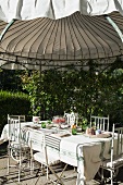 Set table and ornate metal chairs below round roof of climber-covered garden pavilion