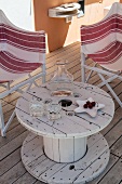 Upcycled table made from old cable reel on wooden terrace between two striped director's chairs