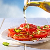 Olive oil being poured over seasoned tomato slices