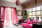 Comfortable sofa with pink scatter cushions and throw in front of lattice window; open terrace doors invite you to walk in the garden