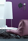 Contemporary designer couch next to white coffee table and minimalist standard lamp against purple wall