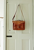 Vintage leather bag hanging from coat hook on white panelled door