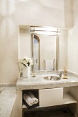 Schlichter Waschtisch aus heller Steinplatte mit eingelassenem Edelstahlbecken und beleuchtetem Spiegel in Wandnische eines orientalischen Bades