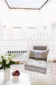 White, wooden, lattice chair with seat cushion in elegant loggia with view into small, bright, Oriental courtyard; closed courtyard doors around walls, eaves of tiled roof and open view of sky