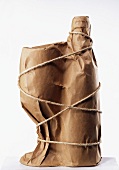 A glass and a bottle wrapped in brown paper and tied with string