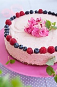 Raspberry mousse layer cake with raspberries, blueberries and flower decoration