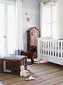 Nostalgic atmosphere in nursery with white cot, rocking horse and large, cubic, velour pouffe; small cupboard with roof against wall painted blue and white