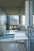 Bathroom with a sunken bathtub in front of a large mirrored wall; the countryside and a sea of houses reflected in the mirror