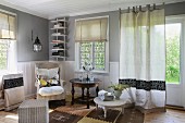 Einfaches Wohnzimmer mit hellgrauen Wänden und weisser Wandverkleidung; in der Ecke ein Lesessel mit weichen Kissen und ein antiker Beistelltisch