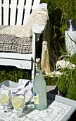 Mit Erfrischungsgetränk gedecktes Tablett vor weißem Gartenstuhl im hohen Gras