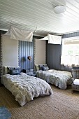 Twin bedroom with cosy fur blankets and scatter cushions on beds below white lengths of fabric used as canopies and upholstered headboards