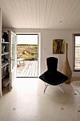 Classic armchair, upholstered in black in front of a open terrace door in a simple living room with white wood ceiling