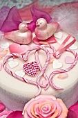 A white cake decorated with hearts, birds, rose petals and a bow