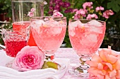 Rosensirup mit Eiswürfeln in zwei Gläsern und Rosenblüten auf einem Tisch im Freien