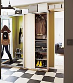 Modern hall with ample storage space in wardrobe with mirrored, sliding door; woman reflected in mirror