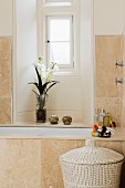 Renoviertes Bad mit hellen Steinfliesen an Wand und Badewanne vor Fensternische mit Blumenstrauss