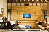 Simple sofa and armchair around glass-topped coffee table in front of wooden partition with integrated TV