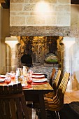 Wooden chairs at set table in front of open fireplace with columns in rustic atmosphere
