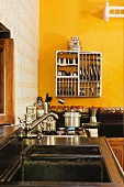 Kitchen counter with vintage tap fittings over sink and crockery in drying rack hung on yellow wall