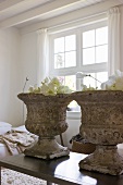 Antique plant pots made of weathered stone on a modern coffee table in a living room with a traditional feel