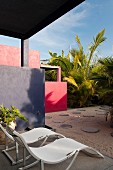 Modern sun loungers on terrace looking out to courtyard with round paving stones and palm plants