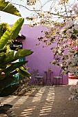 Blick durch Palmen und weißen Bougainvillea auf Tisch für zwei Personen im sandigen Inennhof