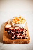 Barbecue Pork Ribs on a Cutting Board with a Bowl of Macaroni and Cheese