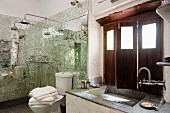 Washstand below window with interior wooden shutters and shower area with mirrored mosaic wall panels