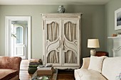 Cupboard with double doors, curved glass panels and curtains in vintage living room with view into bright foyer