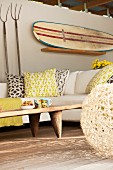 Überdachte Terrasse mit Sofa, Couchtisch aus Holz sowie Gartengeräten & altem Surfbrett als Wanddeko