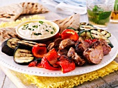 Grillteller mit Lammfleisch, Paprika, Auberginen, Zucchini und Hummus-Dip, dazu Pitabrot
